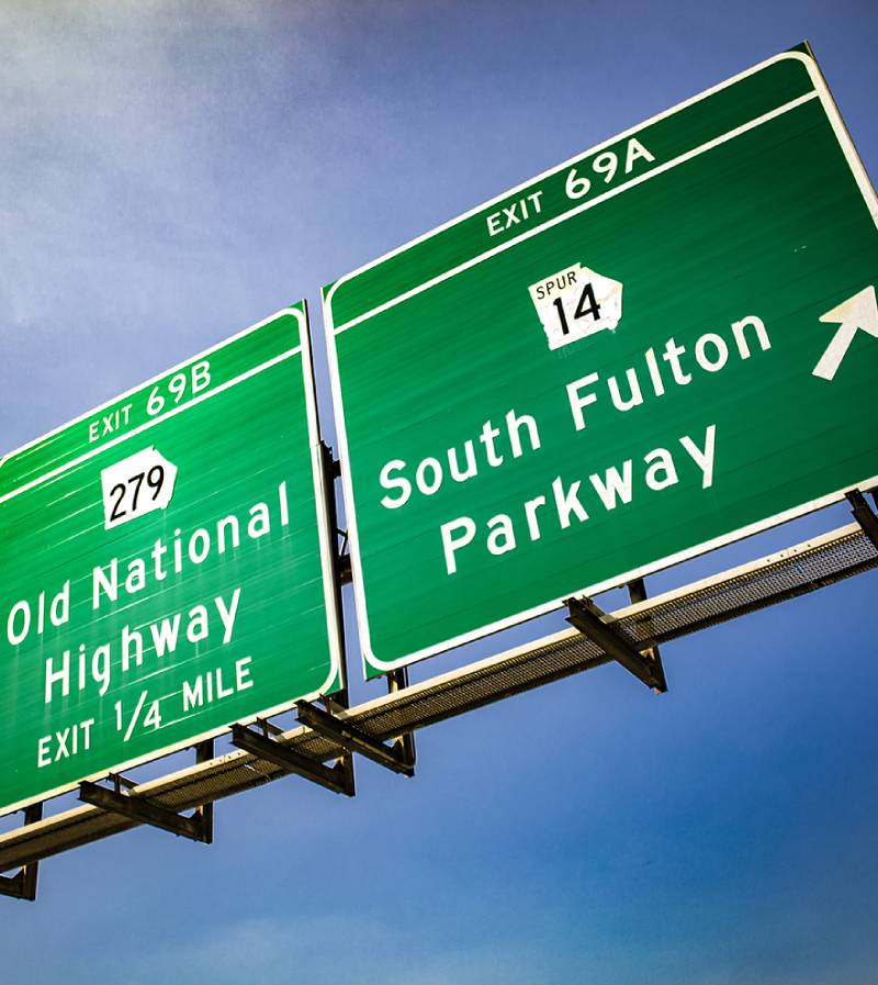 Two green highway exit signs against a blue sky, one pointing to Old National Highway and the other to South Fulton Parkway. Two green highway exit signs against a blue sky, one pointing to Old National Highway and the other to South Fulton Parkway.